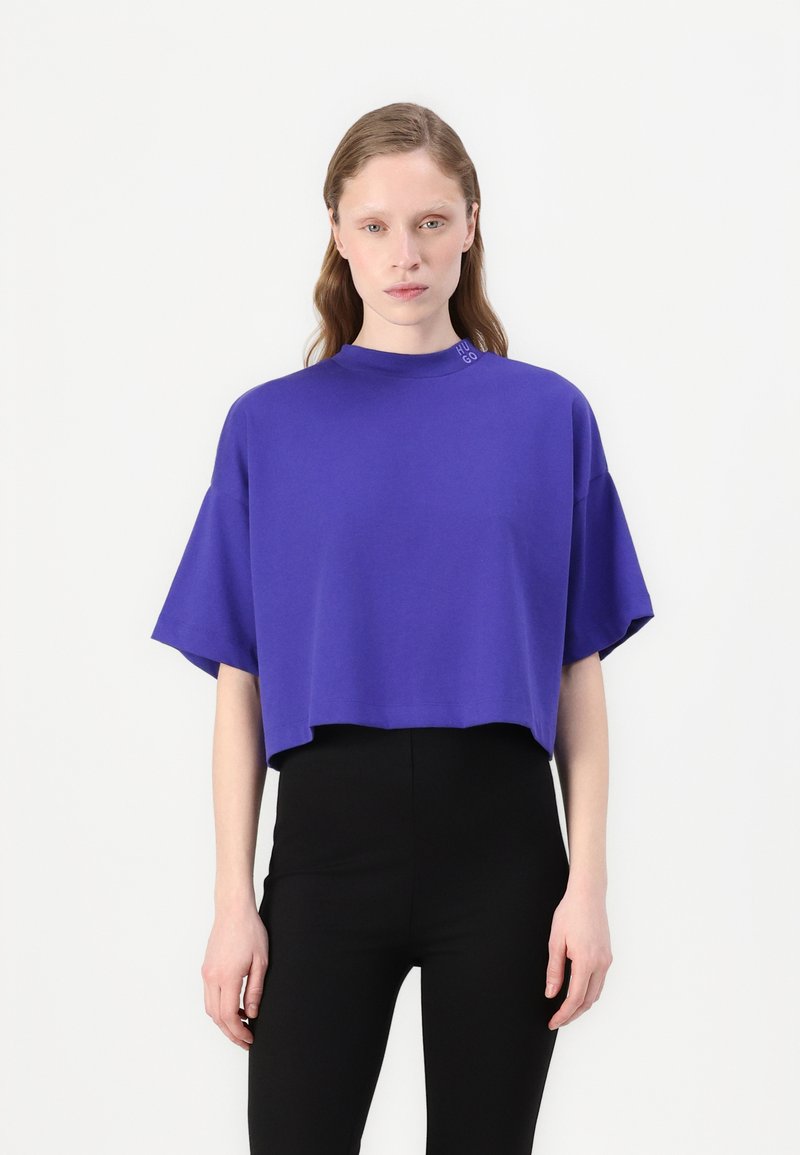 T-shirt corto viola con collo alto e maniche corte. Presenta un dettaglio logo discreto vicino al collo, realizzato in un tessuto morbido.