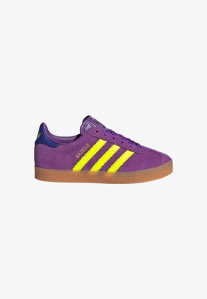 Baskets Adidas Gazelle violettes avec des bandes jaunes, semelle en gomme, languette de talon bleue et lacets violets, vue de côté sur fond blanc.