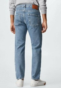 Pantalones vaqueros de mezclilla azul claro con corte de pierna recta, dos bolsillos traseros y un parche de cuero marrón en la cintura. Combinados con zapatillas blancas.