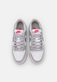 Nike sneakers featuring a white leather upper, grey accents, perforated toe box, and grey laces. Red logo on the tongue and heel.