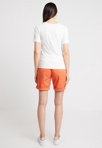 T-shirt bianca a maniche corte abbinata a pantaloni corti arancioni con orlo arrotolato. L'outfit presenta un design semplice e una trama di tessuto liscia.