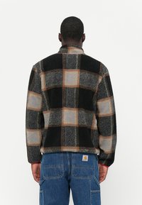 Fleece pulóver s mnohými farebnými kockami v čiernej, sivej a oranžovej farbe. Má vysoký golier a textúrovanú tkaninu.