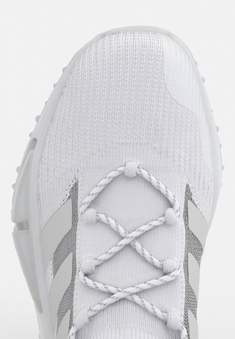 Scarpa sportiva bianca con tomaia in maglia testurizzata, accenti grigi e design con lacci. Caratterizzata da una suola in gomma con piccole scanalature per una migliore aderenza.