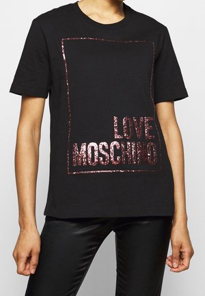 Osoba ubrana w czarną koszulkę z krótkim rękawem z błyszczącym, różowo-złotym napisem "LOVE MOSCHINO" w obrębie kwadratowego obrysu na przodzie.