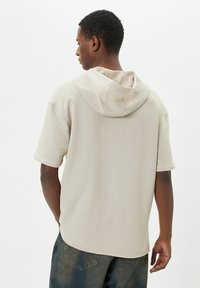 Beige lyhythihainen huppari pehmeällä pinnalla ja kaksikerroksisella hupulla. Ominaisuuksiin kuuluu rento malli ja kaareva helma.