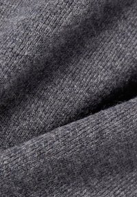 Grau gestrickter Stoff mit einer weichen, strukturierten Oberfläche. Das Material zeigt ein deutliches Muster aus verflochtenen Fasern, das subtile Tiefe erzeugt.