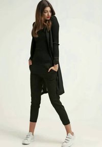 Cardigã longo preto sobre uma blusa preta ajustada e calças pretas justo. Combinado com ténis brancos. Textura suave em todo o outfit.