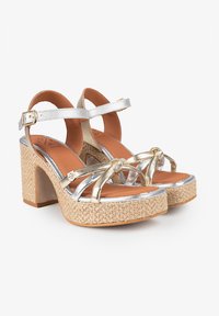 Sandalias de plataforma con tiras doradas y plateadas, base cubierta de yute tejido, tacón cuadrado y correa de tobillo con hebilla. Plantilla suave en tono marrón.