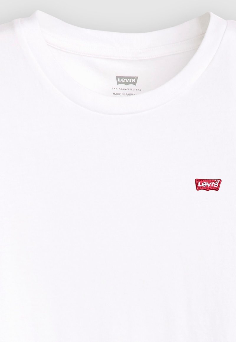 Camiseta de algodón blanca con cuello redondo y un pequeño parche del logo de Levi's en color rojo en la parte izquierda del pecho. Textura suave, diseño casual.