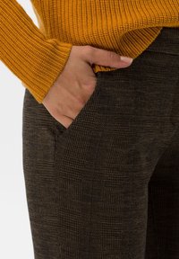 Pantalon à carreaux marron avec une finition texturée, doté d'une poche latérale et associé à un pull côtelé moutarde.