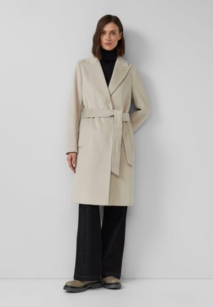 Manteau en mélange de laine beige avec une taille ceinturée, un col cranté, des manches longues et des poches latérales, associé à un pantalon noir à jambes larges et des bottes épaisses.