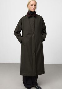 Cappotto lungo di un verde scuro, con collo in corduroy bordeaux. Presenta una vestibilità dritta, tasche laterali e una texture di tessuto morbida.