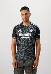 Svart fotballdrakt med et kartlignende mønster, hvit "UNIBET" logo og Adidas merke. Korte ermer og rund hals.