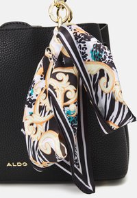 Black textured leather handbag with a gold chain handle. A patterned scarf in black, white, and gold is tied to the side.