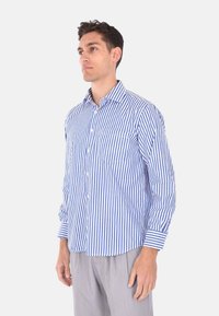 Camicia a maniche lunghe a righe blu e bianche con colletto button-down e taschino sul lato sinistro del petto. Tessuto leggero con una vestibilità comoda.