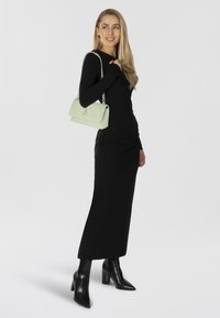 Abito nero a maniche lunghe, aderente in vita, abbinato a stivaletti neri con tacco. Porta una borsa verde chiaro con tracolla a catena.