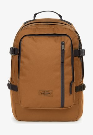 Brauner Stoff-Rucksack mit schwarzen Reißverschlussakzenten, gepolsterten Trägern, einem oberen Griff und einer vorderen Reißverschlusstasche. Mit Logopatch an der unteren Front.