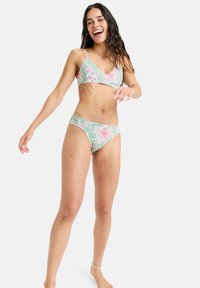 Zestaw bikini w kwiaty, wykonany z zielonego materiału z różowymi wzorami. Górna część ma cienkie ramiączka, a dolna część ma klasyczny krój i szeroki pas.