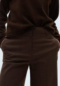 Hnědé texturované kalhoty s jemným kostkovaným vzorem, s bočními kapsami a slim fit střihem, spárované s odpovídajícím jemně hnědým svetrem.