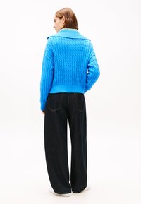 Pulover albastru tricotat cu guler cu reiaturi, având un model texturat și croială scurtă, asortat cu blugi evazați de culoare închisă.