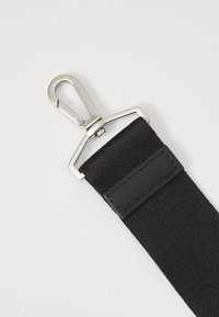 Sangle en nylon noir avec un crochet pivotant en métal argenté et un accent en cuir noir. La sangle présente une surface texturée et des détails cousus.