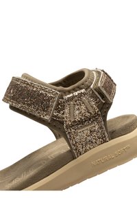 Glittriga beige sandaler med en texturerad fotbädd, justerbara remmar och ett mjukt, naturligt material för komfort. "NATURAL SOFT™" präglat på sulan.