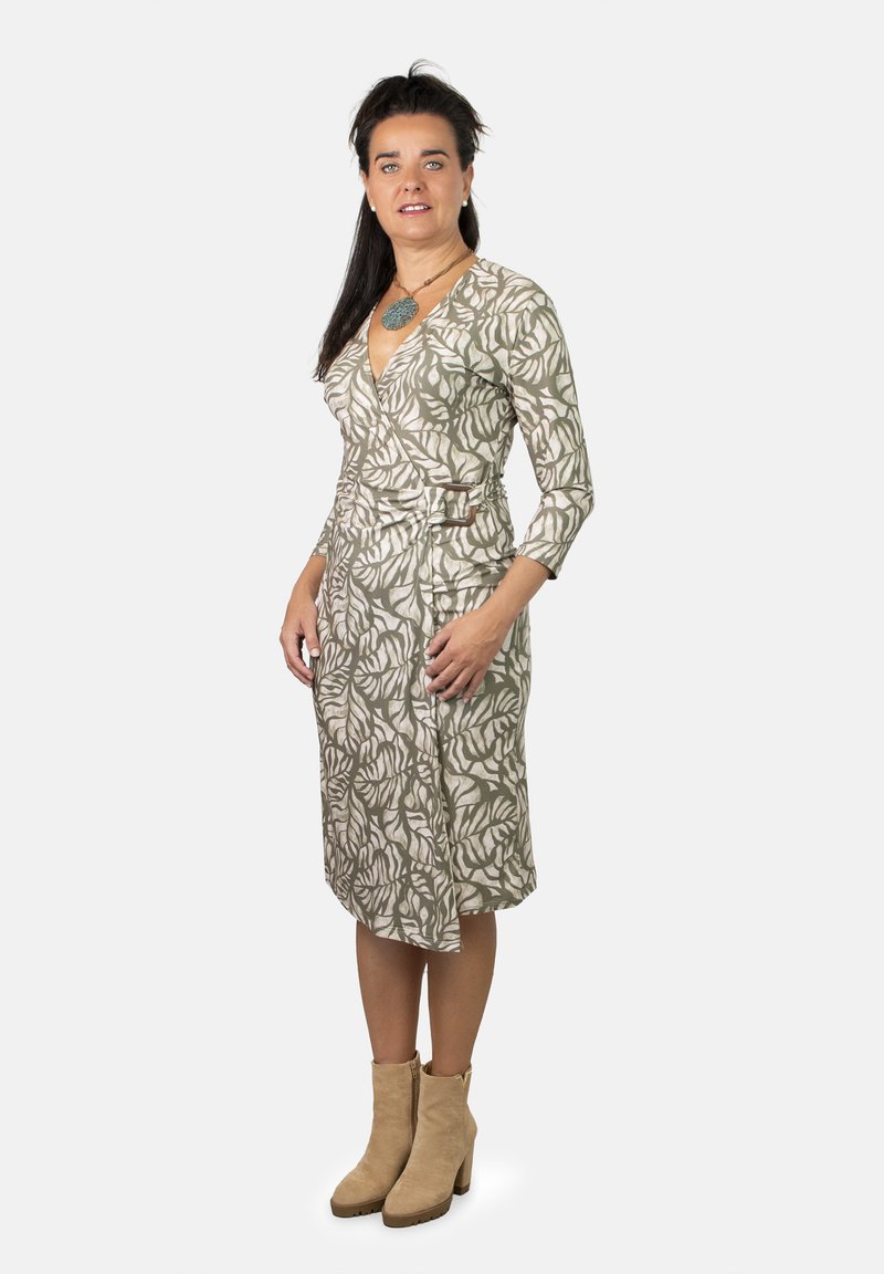 Vestido envolvente con un estampado de hojas en beige y verde, mangas tres cuartos, cintura ceñida con cinturón, largo hasta la rodilla, combinado con botas de tobillo beige.