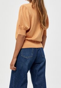 Maglione a maglia pesca con maniche corte a sbuffo, orlo a coste, abbinato a jeans a gamba larga blu scuro con vita alta e tasche posteriori.