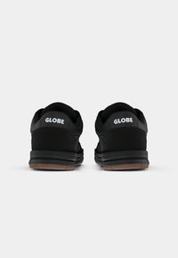 Fekete sportcipők sima felülettel, hátul a "GLOBE" logóval és gumitalppal. Egyszerű, lekerekített formájú design.