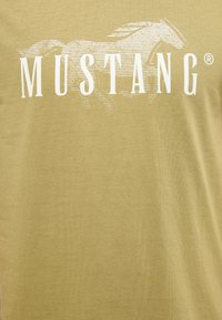 Tkanina w kolorze musztardowo-żółtym z białym napisem "MUSTANG" na tle zarysu galopującego konia z liniami.
