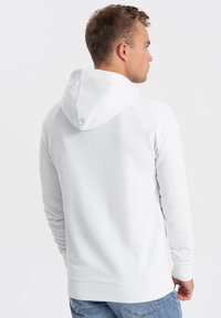 Sudadera de forro polar blanca con capucha forrada, puños y dobladillo acanalados. Presenta una textura suave y un corte clásico y relajado.