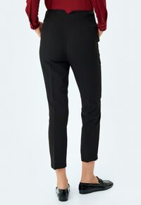 Pantalons noirs ajustés à taille haute et coupe slim, dotés de pinces arrière et d'une longueur aux chevilles, fabriqués en tissu tissé.