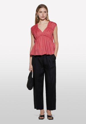Korallenfarbener Peplum-Top mit gefaltetem Design und V-Ausschnitt, kombiniert mit hochgeschnittenen schwarzen weiten Hosen und schwarzen Riemchensandalen.