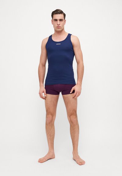 Marineblaues Tanktop mit rundem Ausschnitt und einfarbigem Material, mit einem kleinen weißen Logo. Kombiniert mit kastanienbraunen Boxershorts.