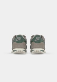 Nike kedas pelēkā zvejā ar zaļiem akcentiem. Iezīmēts ar polsterētu apkakli, logo uz mēles un teksturētu baltu gumijas zoli.