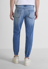 Joggers de mezclilla azul claro con puños elásticos y dos bolsillos traseros. La tela tiene un acabado ligeramente desgastado y un corte relajado.