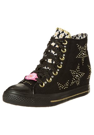 Czarny sneakers na koturnie z złotymi ćwiekami w kształcie gwiazdy, czarno-białym wzorzystym językiem, złotymi oczkami i różową naszywką z logo na sznurowadłach.