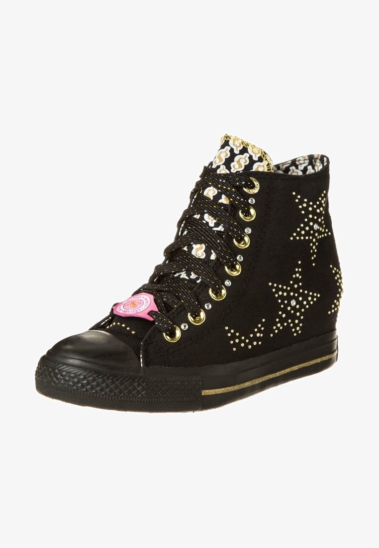 Basket à compensée noire avec des clous étoiles dorés, une languette noire et blanche à motif, des œillets dorés et une étiquette logo rose sur les lacets.