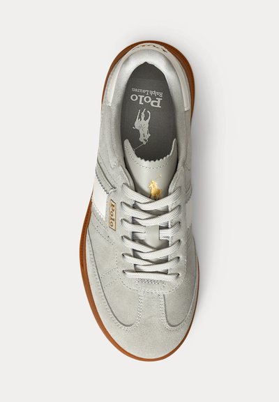 Pilka zomšinė sportinė avalynė su balta odine juostele, baltais raišteliais, ruda guminė pado dalimi ir auksiniu Polo Ralph Lauren logotipu ant liežuvio ir šono.