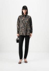 Camicia con stampa leopardata nera e dorata, con bottone frontale, maniche lunghe e vestibilità ampia, abbinata a pantaloni aderenti neri e tacchi neri con cinturini.