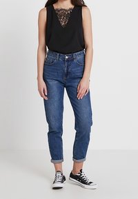 Svart ärmlös topp med spetsdetaljer, paired med ljusblå denimjeans som är uppvikta vid fållen, och svarta canvas sneakers.