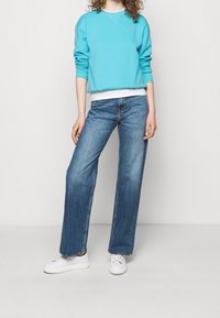 Světle modrý svetr s kulatým výstřihem a logem na hrudi, doplněný volnými modrými jeansy a bílými teniskami. Jednoduchý design.