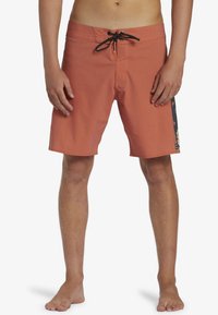 Shorts de bain pour homme en corail, en tissu léger, avec un cordon noir. Présente un motif floral sur le côté. Longueur mi-cuisse.