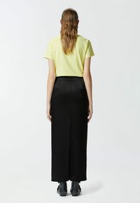 Žuta uska majica, crna duga suknja s prorezom na leđima i crne gležnjače. Glatke teksture, jednostavan dizajn, minimalni detalji i čiste linije.