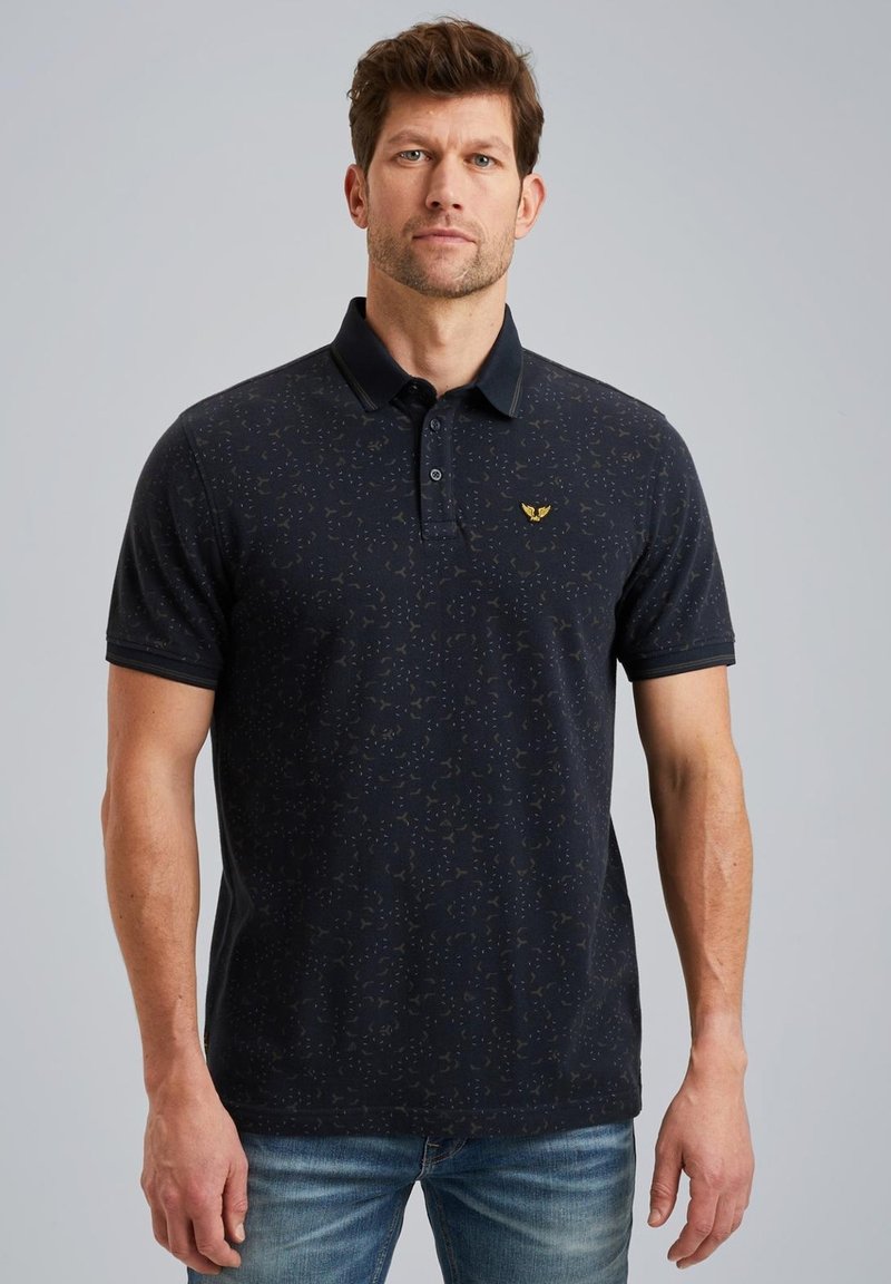 Polo de color navy con un patrón sutil, de manga corta y cuello tipo polo. Presenta un logo dorado en el pecho. Textura de tela suave.