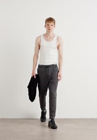 Herreoutfit med en hvid tanktop, grå sweatpants med snoretræk og sorte sneakers, der holder en sort jakke. Simpelt design.