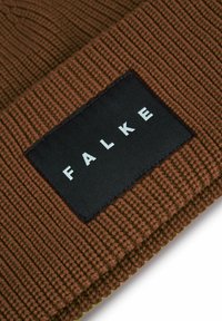 Cappello a cuffia marrone lavorato a maglia con texture a coste e una toppa logo nera con la scritta "FALKE". Il design presenta un risvolto arrotolato nella parte inferiore.