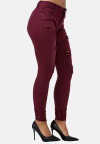 Jeans ajustados burdeos con desgastes y dobladillos deshilachados, hechos de tela elástica, combinados con zapatos de tacón negro.