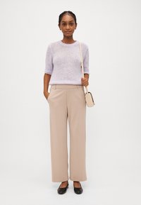 Light purple short-sleeve knit sweater, beige wide-leg trousers, and black flats. Model holds a beige crossbody bag. Smooth texture.