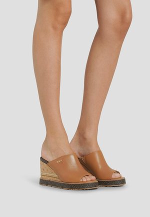 Hnědé kožené sandály na klínu s korkovým podpatkem, otevřenou špičkou a texturovanou černou podrážkou s vzorovaným detailem.